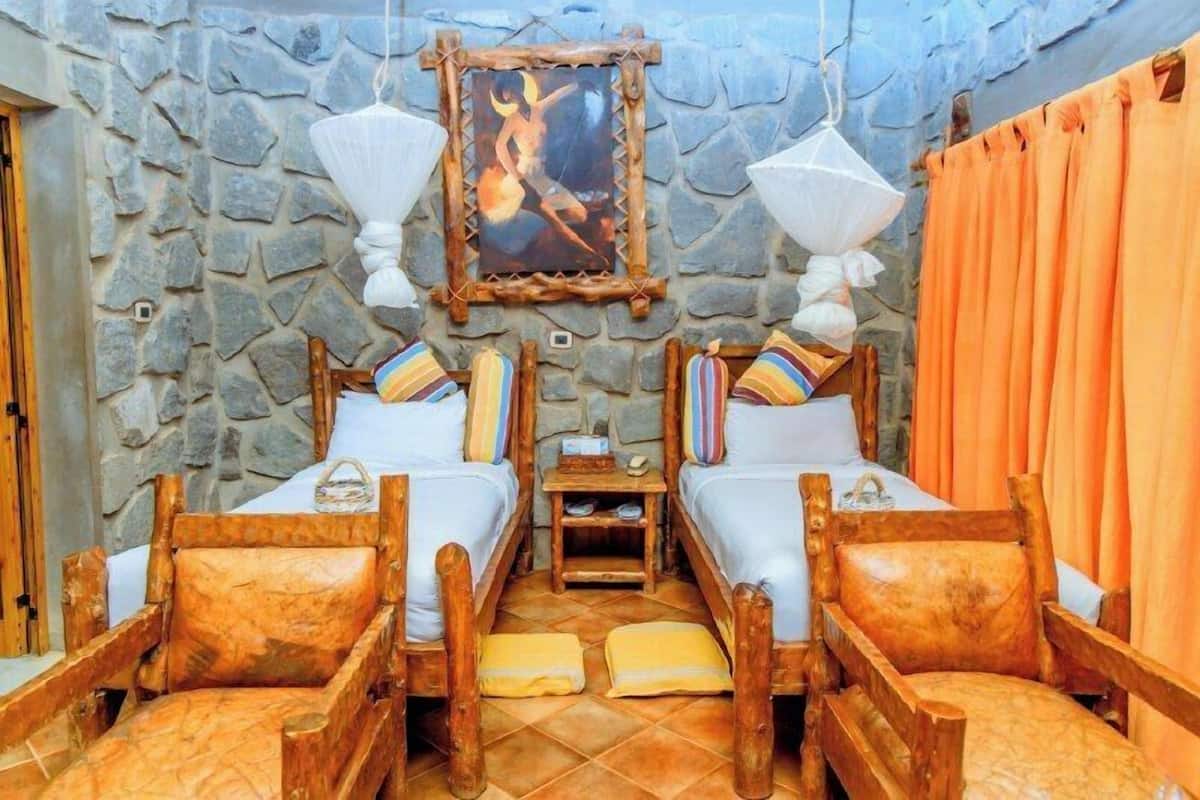 Une chambre avec deux lits en bois, des murs en pierre et un tableau accroché au-dessus des lits.