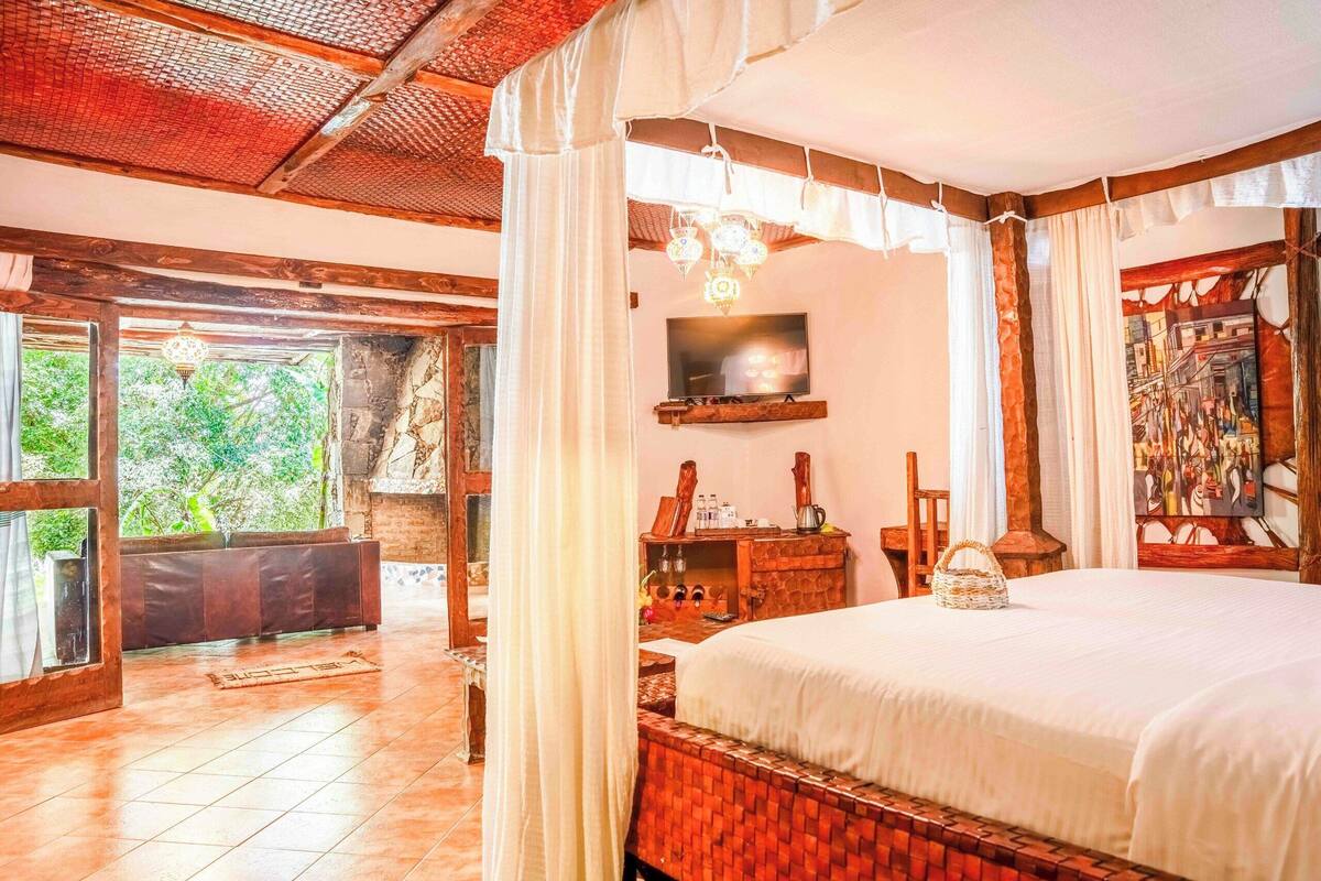 Une chambre dotée d’un grand lit, d’une télévision, d’une commode en bois et d’une fenêtre donnant sur un paysage verdoyant.