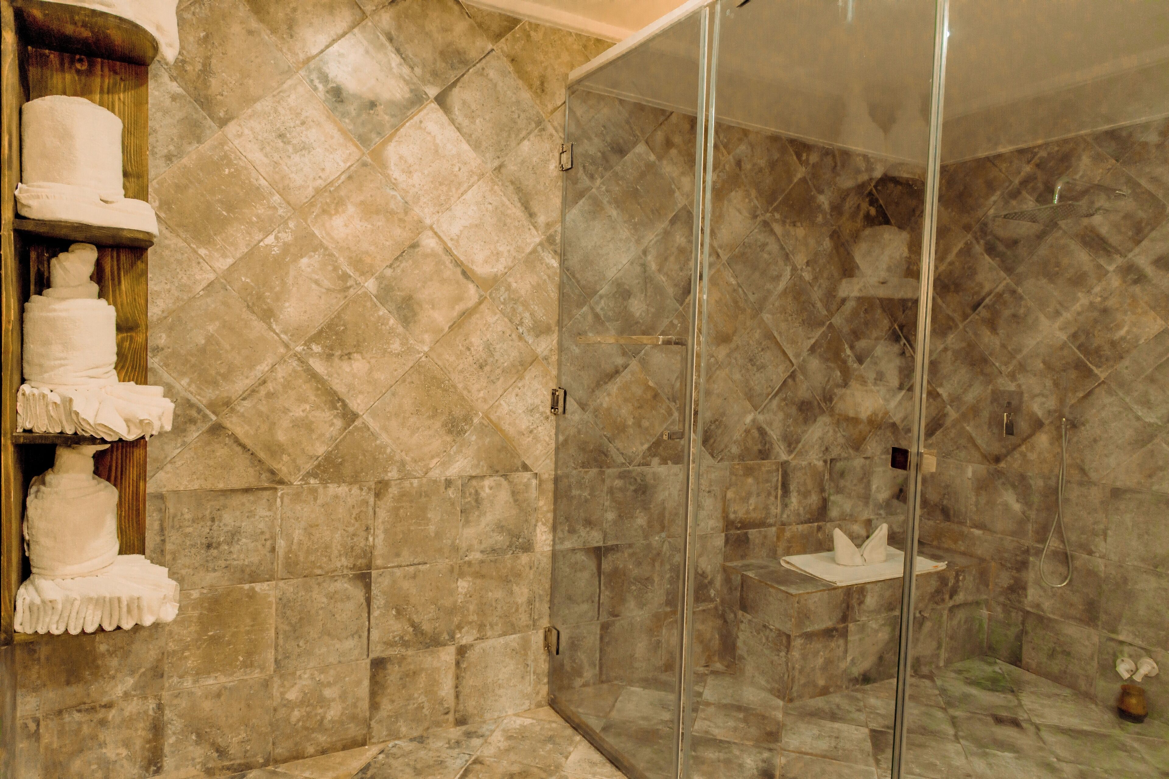 Un espace douche doté d’une porte en verre, de carreaux de marbre et d’une étagère où sont pliées des serviettes.