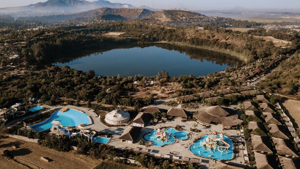 Luchtbeeld van een resort met een groot meer, verschillende zwembaden en constructies met rieten daken.