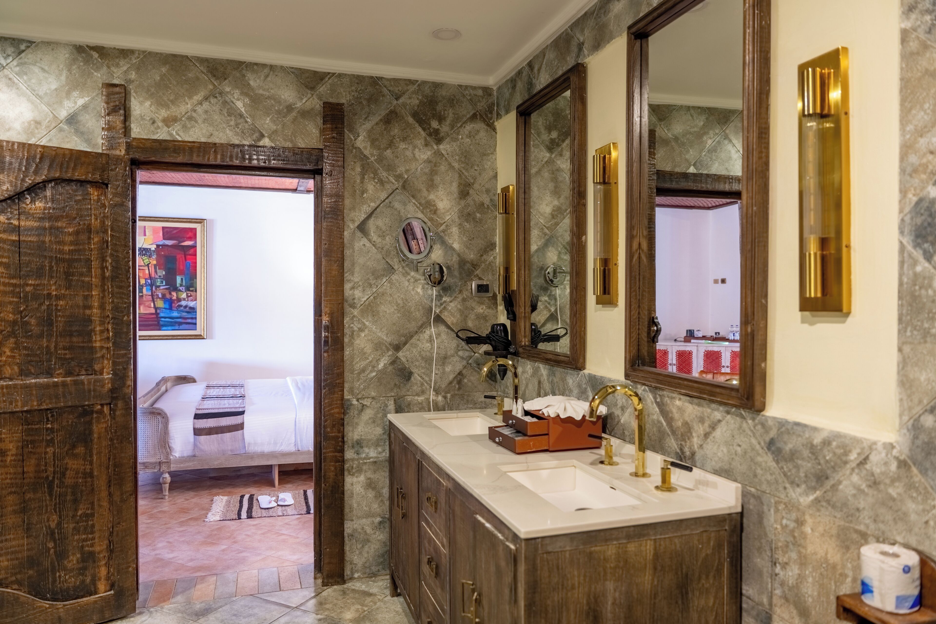 A bathroom with a marble wall, a wooden vanity, two sinks, and a large mirror.