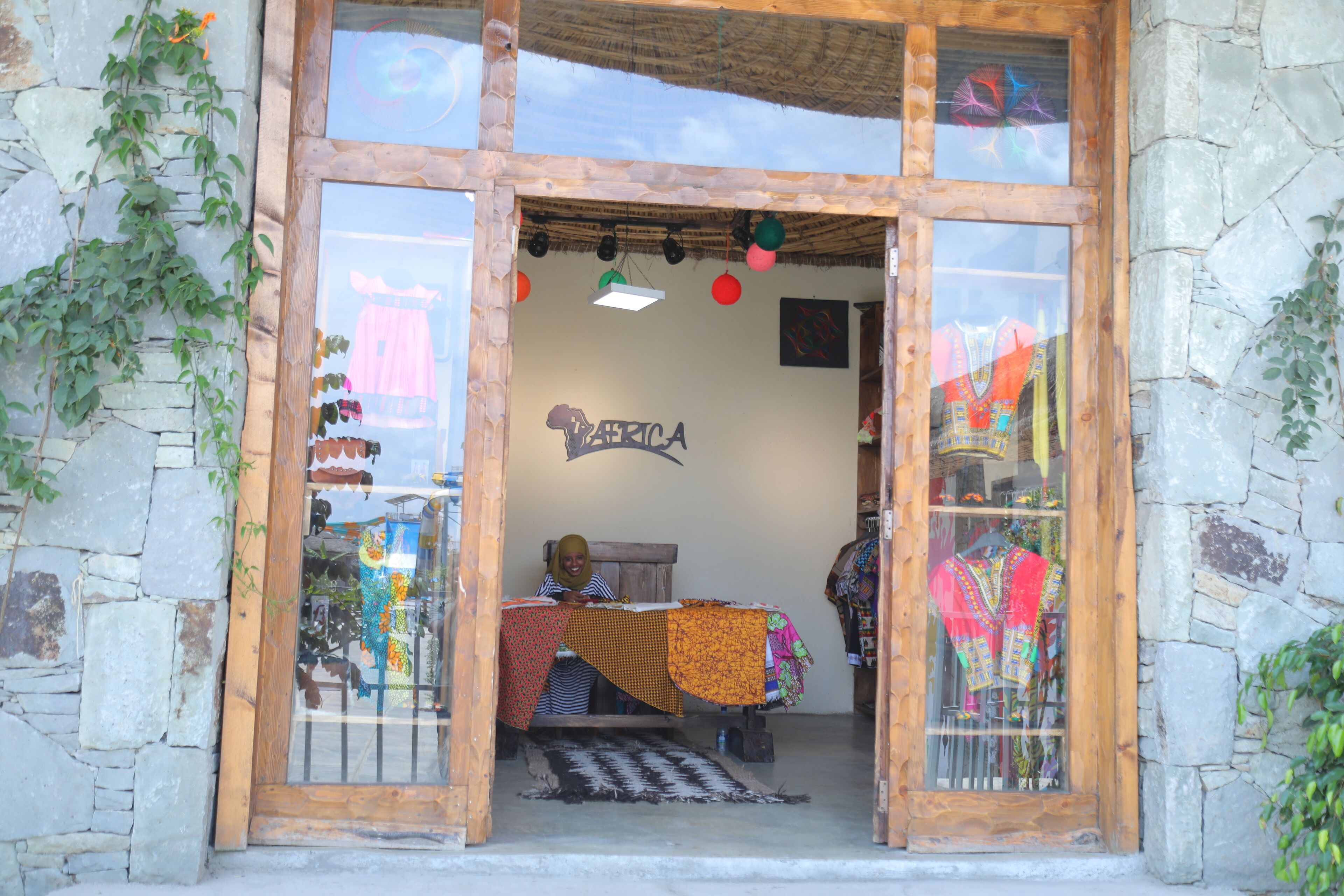 A storefront with a wooden frame, a sign reading "America," and various colorful textiles displayed outside.