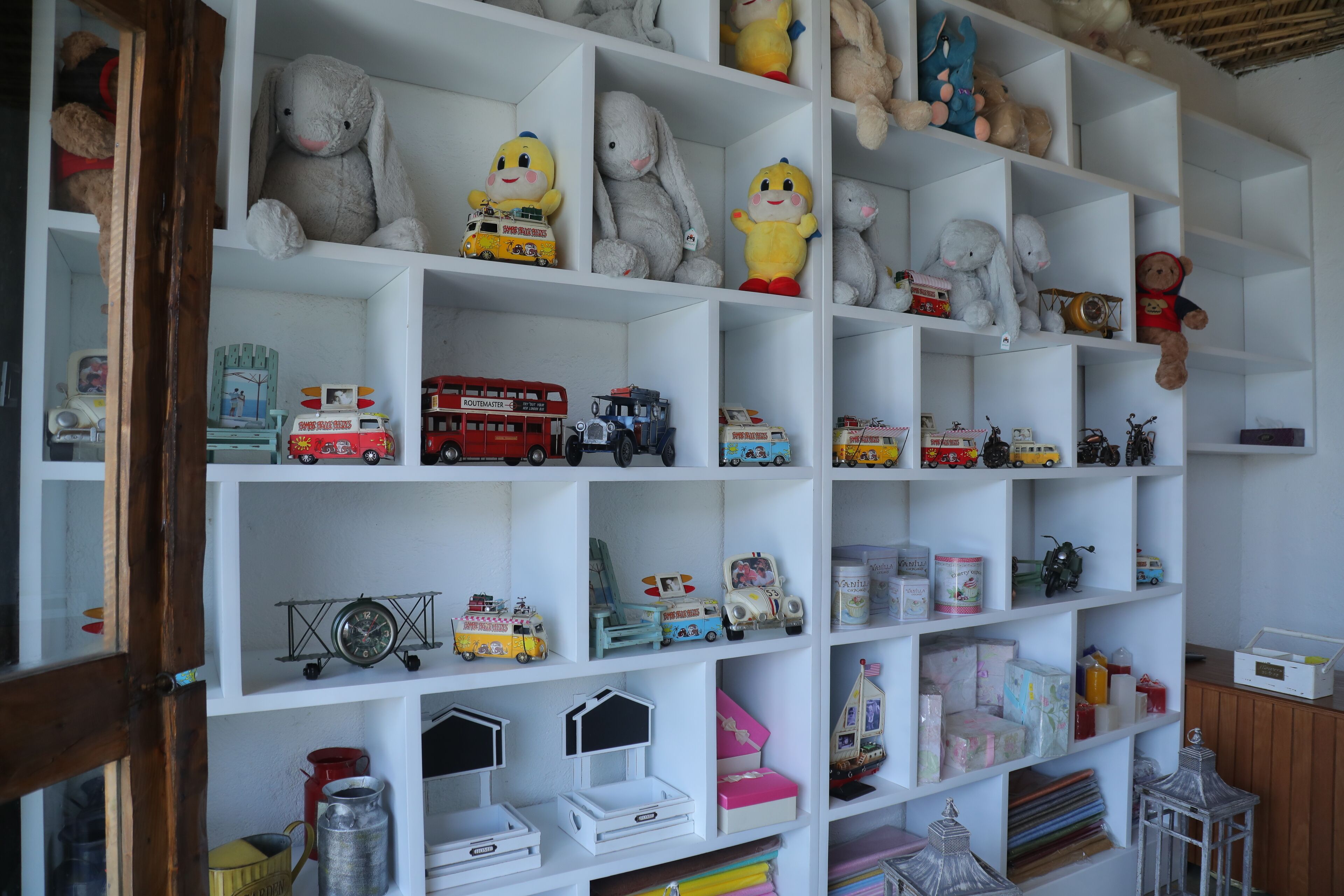 A room with white shelves filled with various toys, including stuffed animals and toy vehicles.