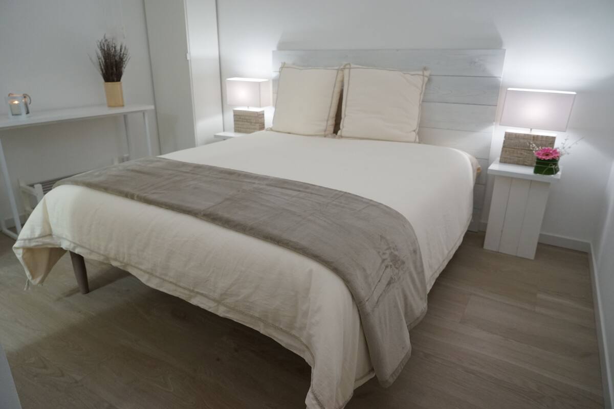 Ein modernes Schlafzimmer mit einem großen Bett, Nachttischen mit Lampen, einem Regal mit dekorativen Gegenständen und Holzboden.