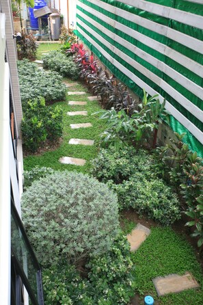 Un étroit sentier de jardin, bordé de pierres plates permettant de traverser, et entouré de divers arbustes et plantes.