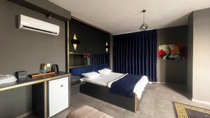 Een moderne hotelkamer met een bed, een bureau, een kleine kitchenette en een groot raam met gordijnen.