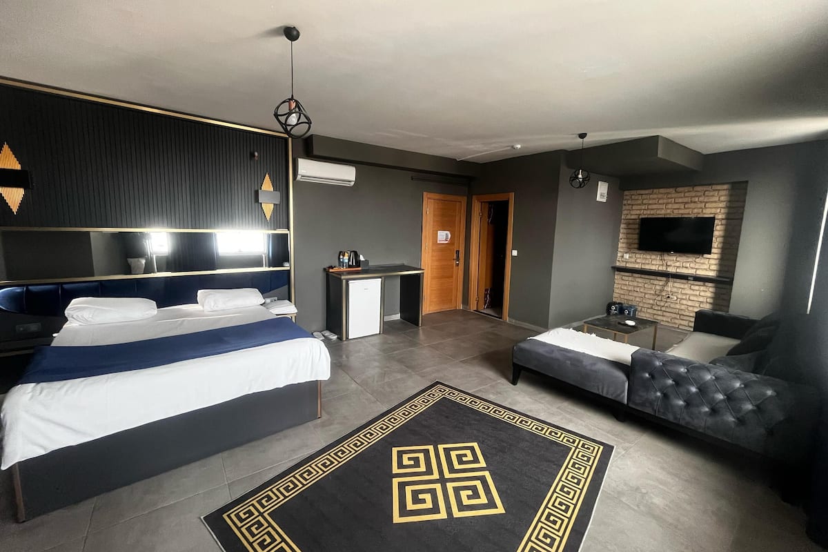 A hotel room with a bed, a sofa, a desk, a TV, and a patterned rug.