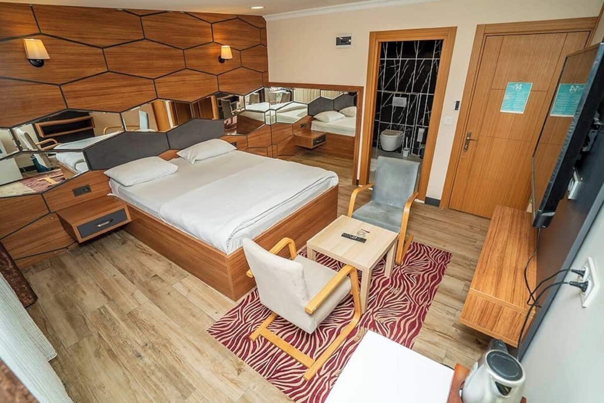 A compact hotel room with a bed, bedside tables, a chair, a small desk, and a television.