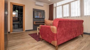 Een woonkamer met een rode bank, een televisie en een houten vloer.