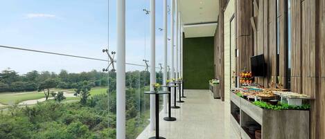 Un pasillo con vista a un campo de golf, un bufé con diferentes platillos y un televisor montado en la pared.