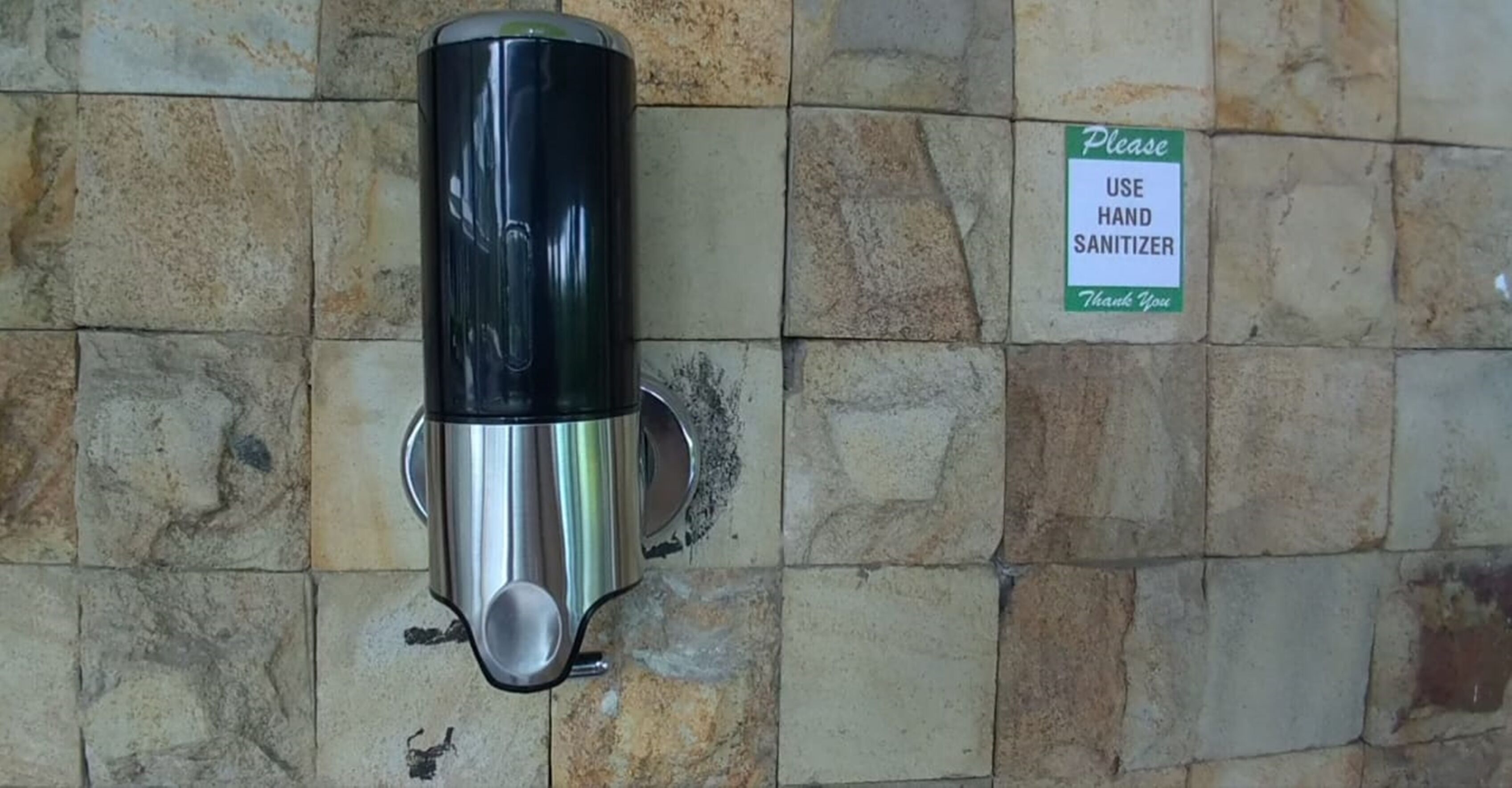 A hand sanitizer dispenser mounted on a stone wall.