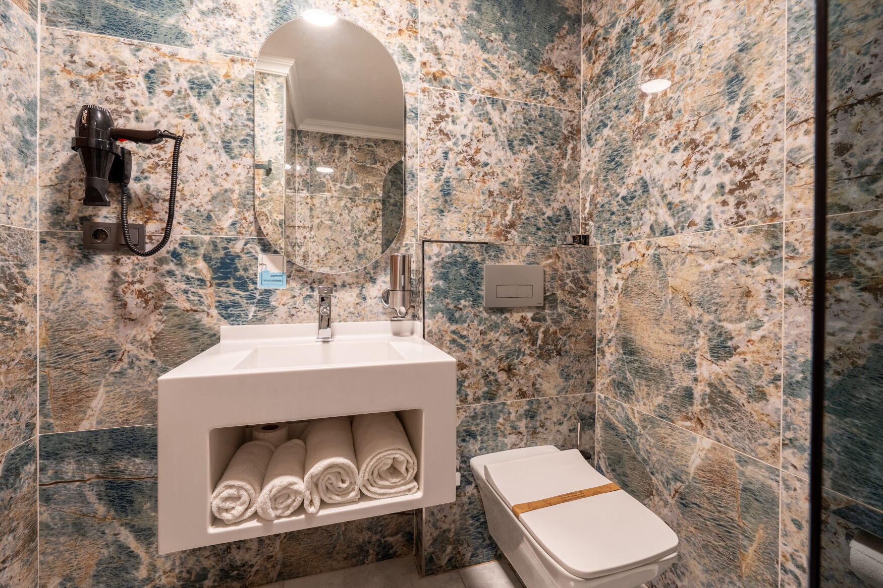A bathroom with a marble wall, a sink with a towel rack, and a toilet.