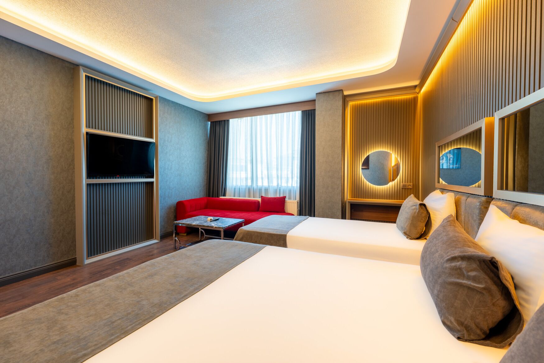 A hotel room with a bed, a red sofa, a small table, and a TV.