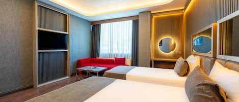Habitación de hotel con cama, sofá rojo, una mesita y televisor.