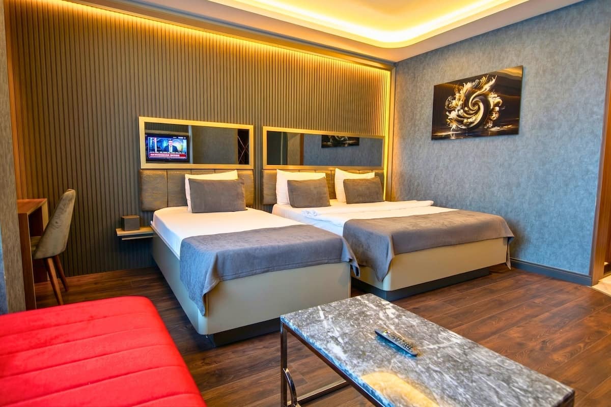 A hotel room with two beds, a TV, a red sofa, and a marble table.