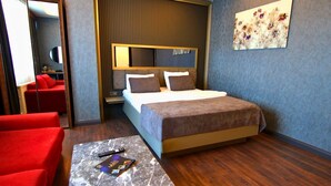 A hotel room with a bed, a red sofa, a small table with a remote control, and a painting on the wall. -  216 Eagle Palace Suite (Istanbul)