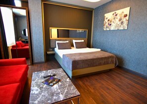 A hotel room with a bed, a red sofa, a small table with a remote control, and a painting on the wall. -  216 Eagle Palace Suite (Istanbul)