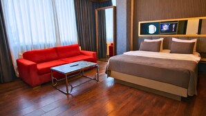 A hotel room with a red sofa, a bed with a grey duvet, wooden flooring, and a television on the wall. -  216 Eagle Palace Suite (Istanbul)