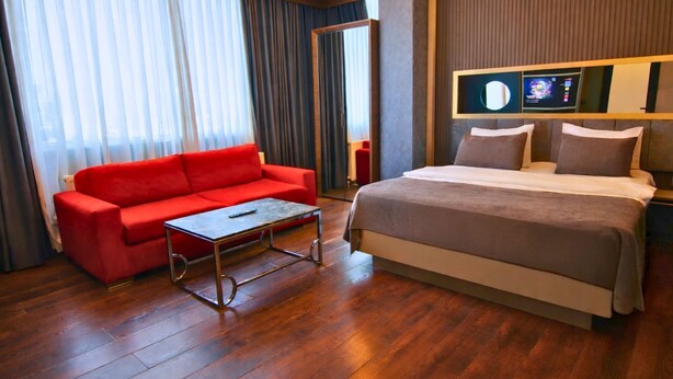 A hotel room with a red sofa, a bed with a grey duvet, wooden flooring, and a television on the wall. -  216 Eagle Palace Suite (Istanbul)