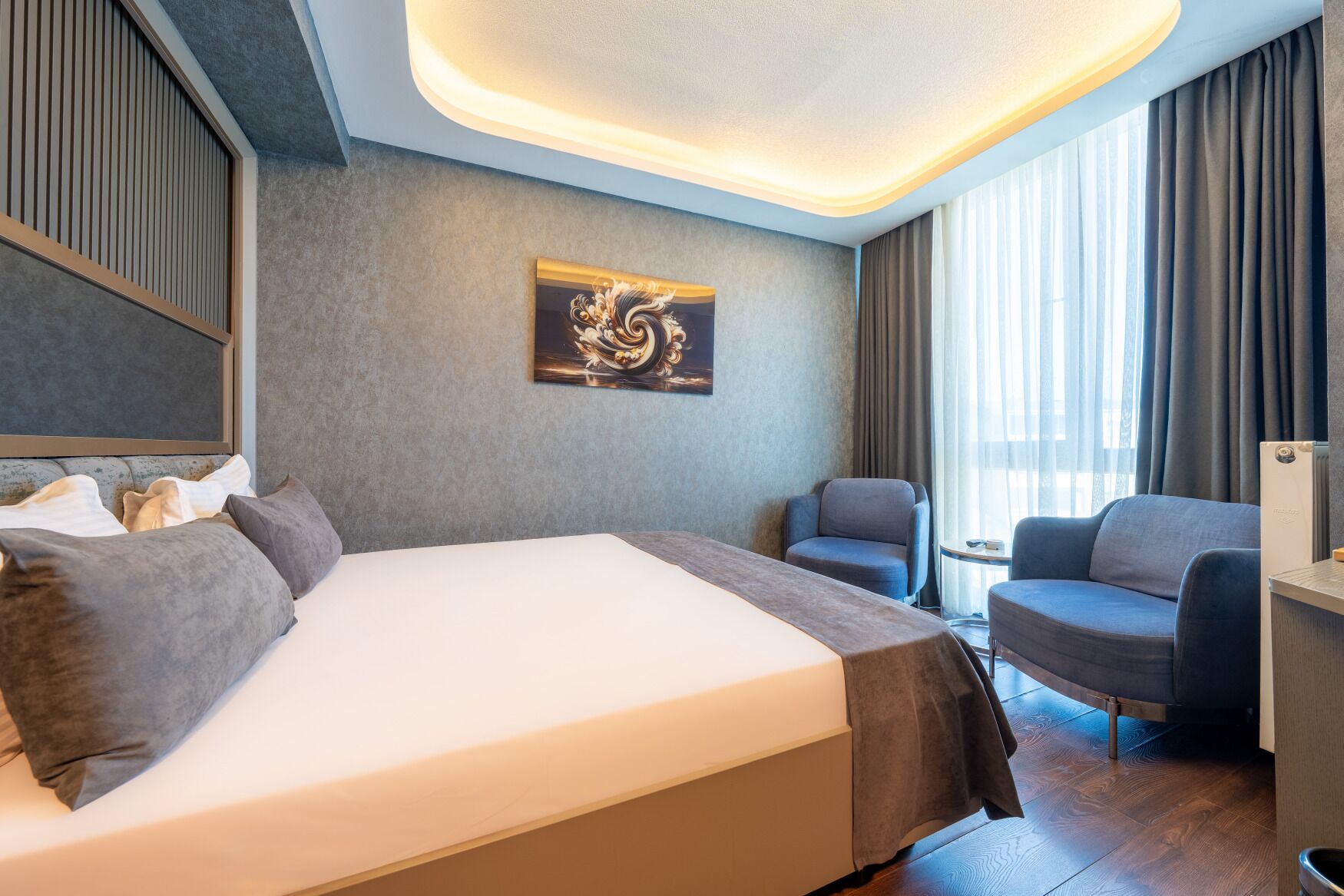 A hotel room with a large bed, a chair, a small table, and a radiator.