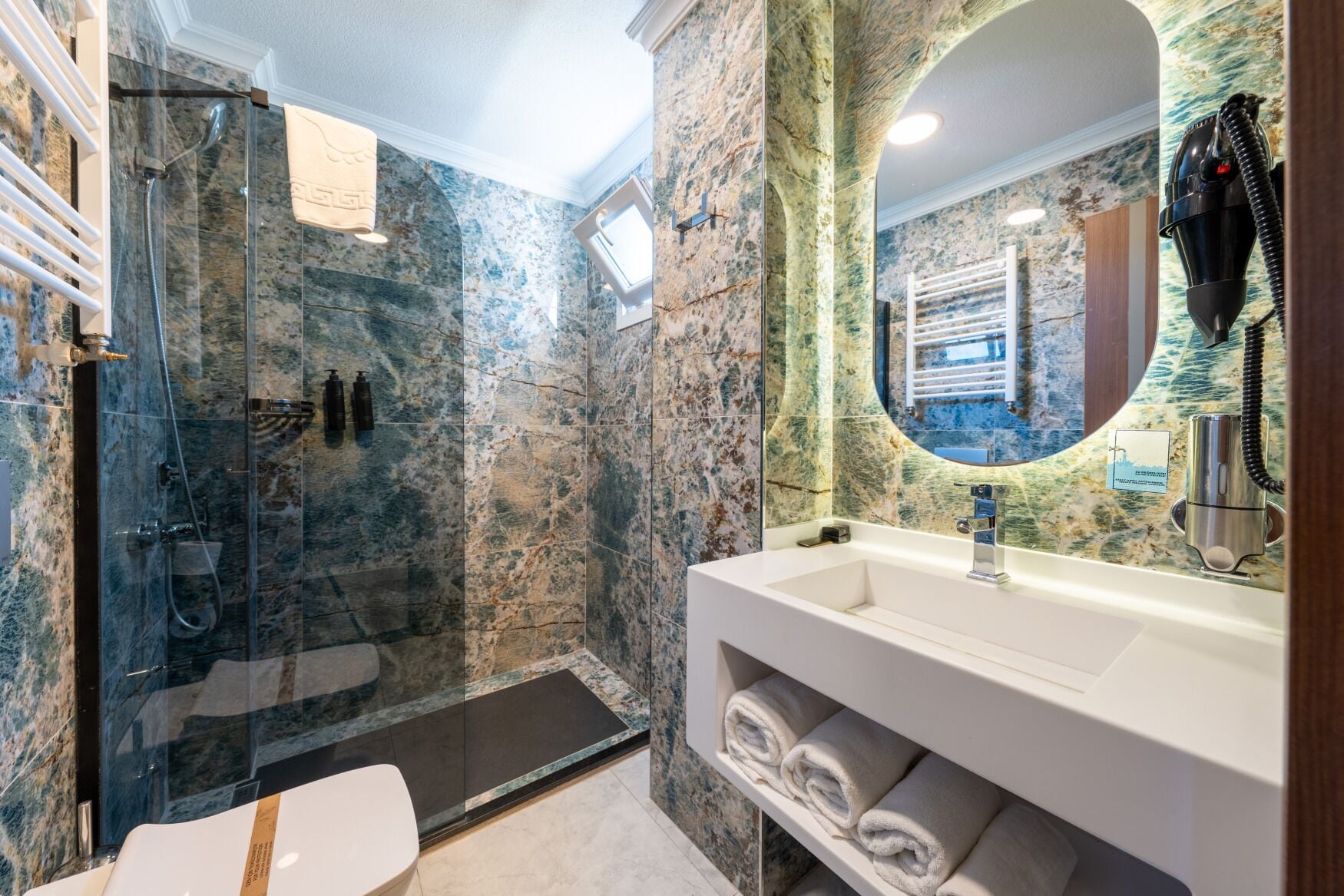 A modern bathroom with a glass-enclosed shower, a white sink, and a marble wall.