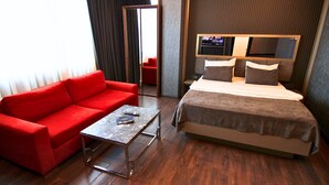 A hotel room with a red sofa, a small table, a bed with a TV above it, and a wooden floor. -  216 Eagle Palace Suite (Istanbul)
