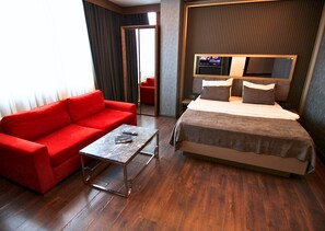 A hotel room with a red sofa, a small table, a bed with a TV above it, and a wooden floor. -  216 Eagle Palace Suite (Istanbul)