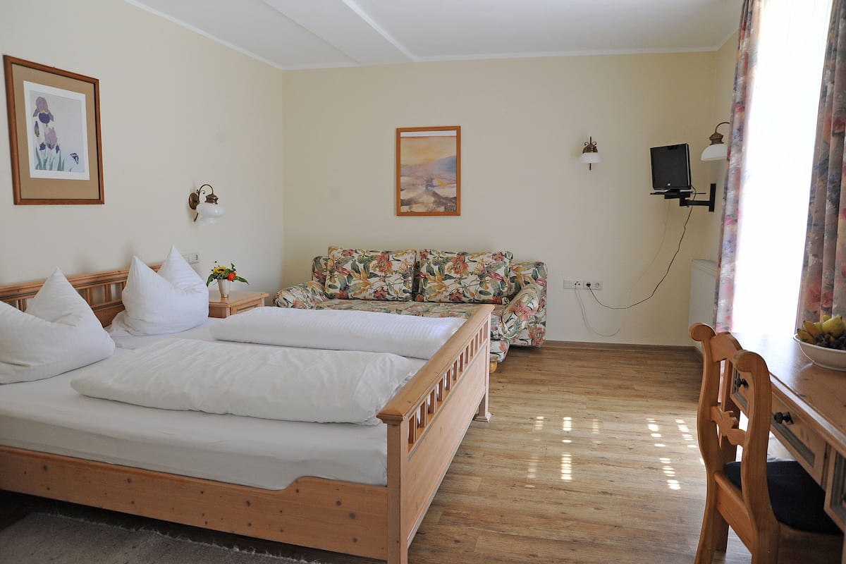 A room with a wooden bed, a sofa, and a TV.