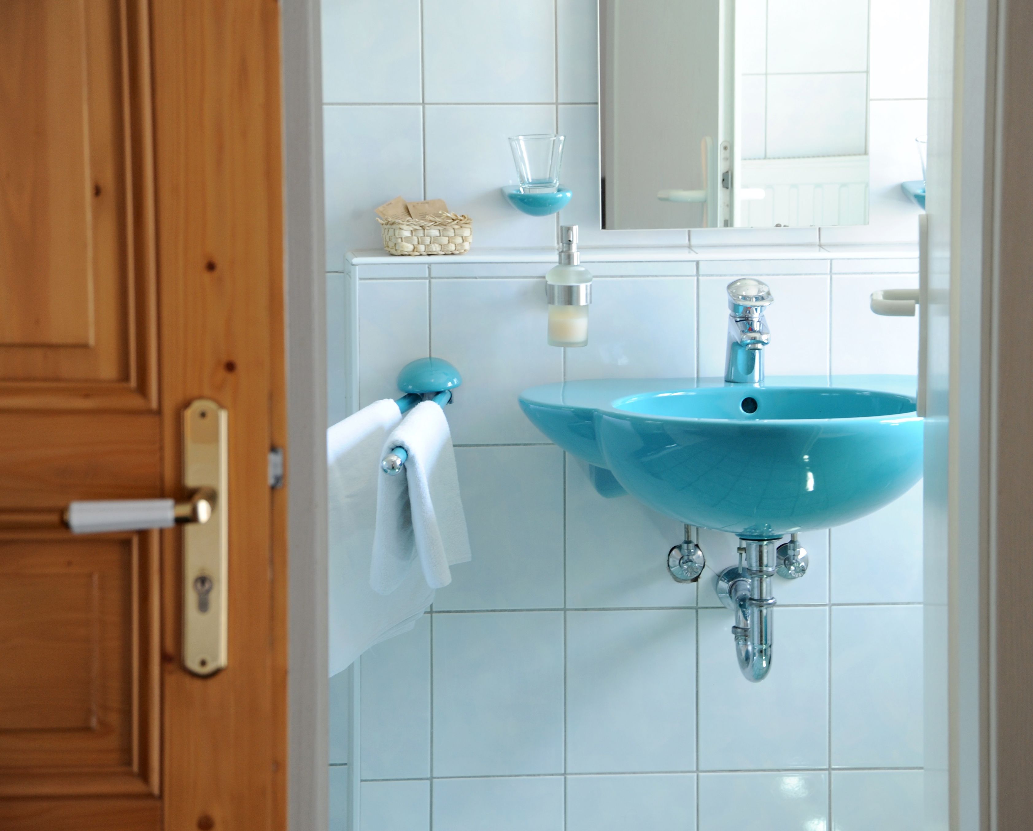 A bathroom with a blue sink, white tiles, a wooden door, and a mirror.