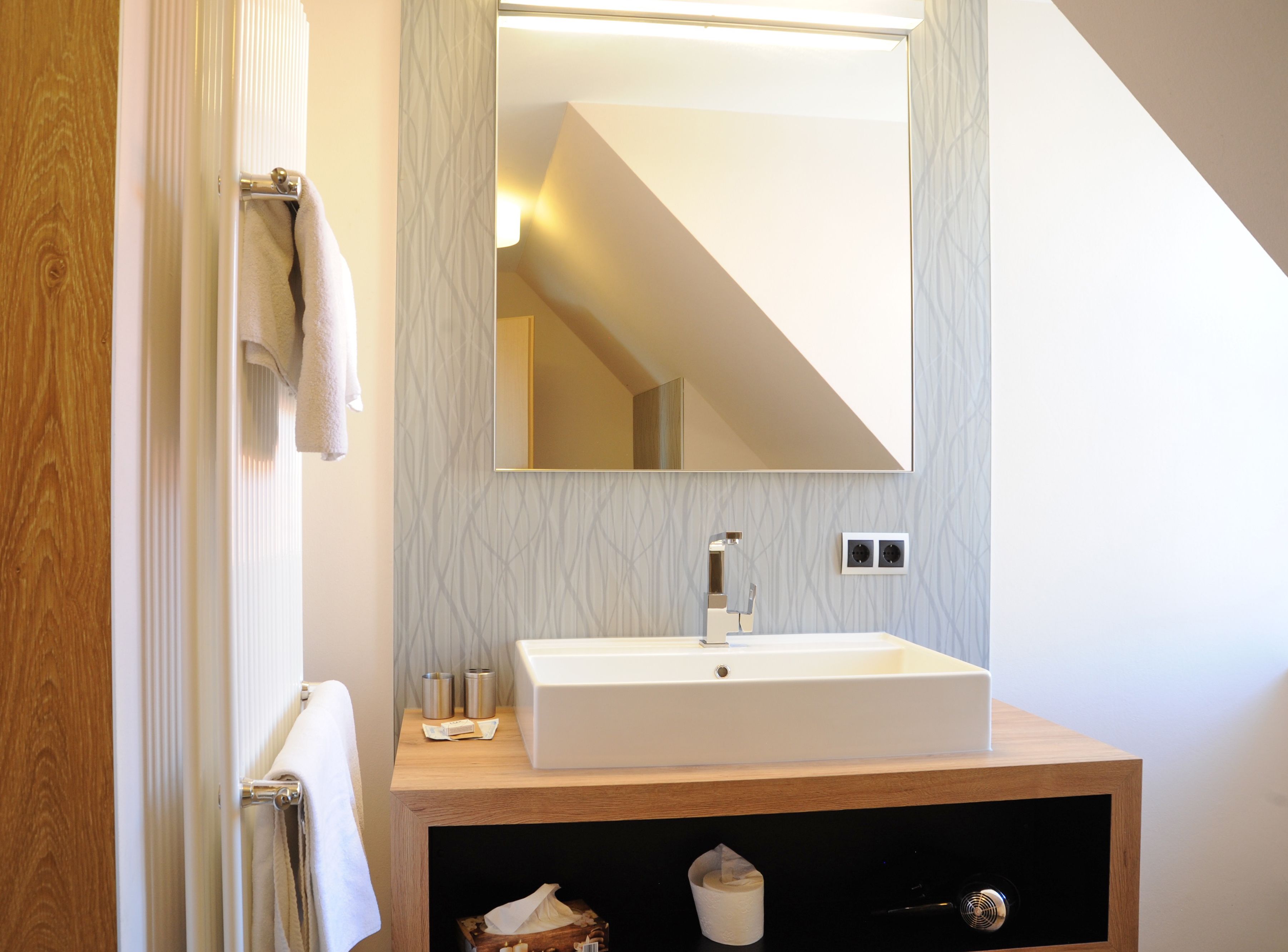 Un baño moderno con tocador de madera, un espejo grande y un perchero para toallas.