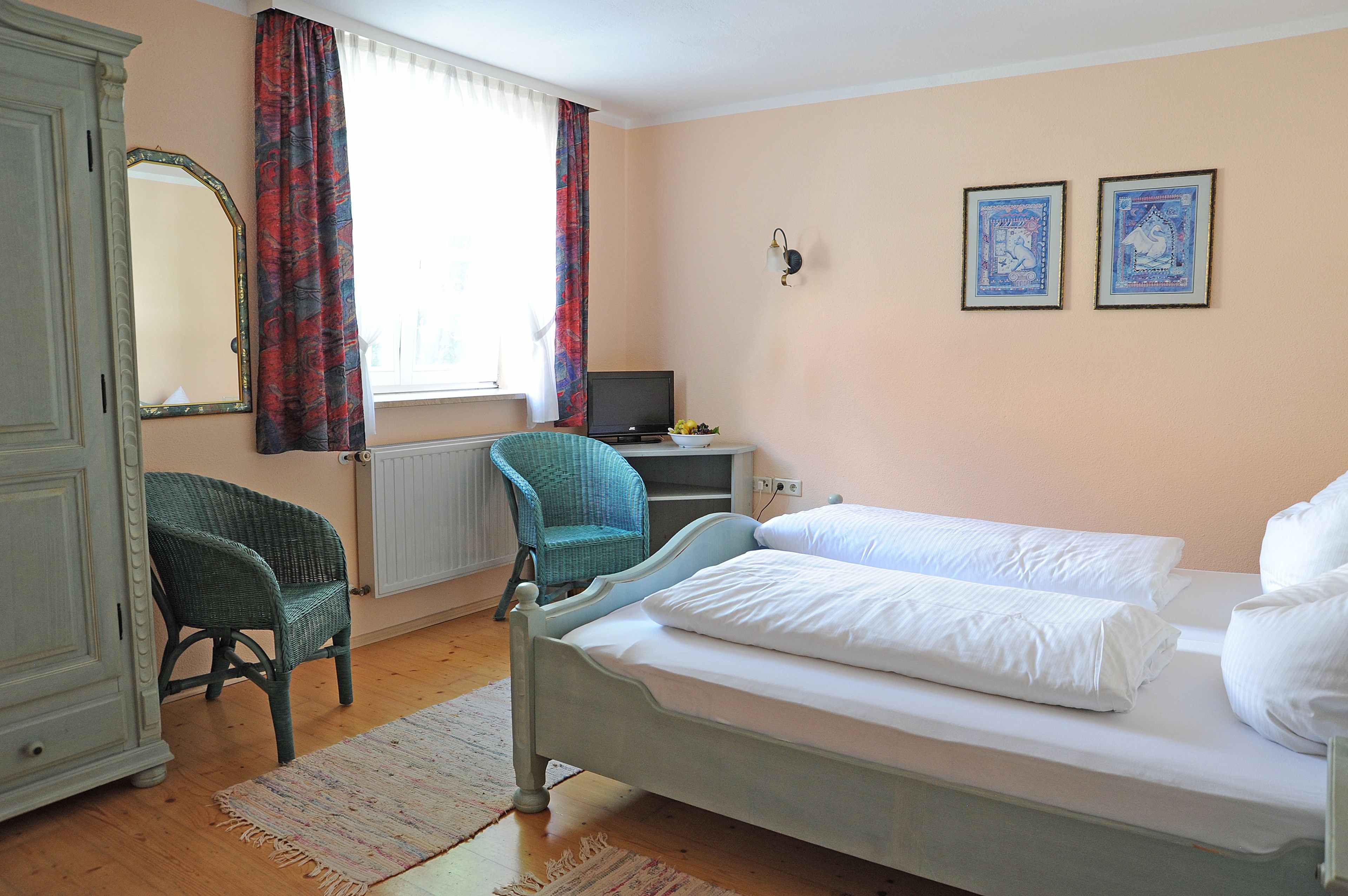 A bedroom with a bed, a chair, a desk, a television, and two framed pictures on the wall.