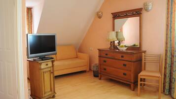 A room with a television on a wooden cabinet, a sofa, a wooden dresser, a chair, and a mirror on the wall.
