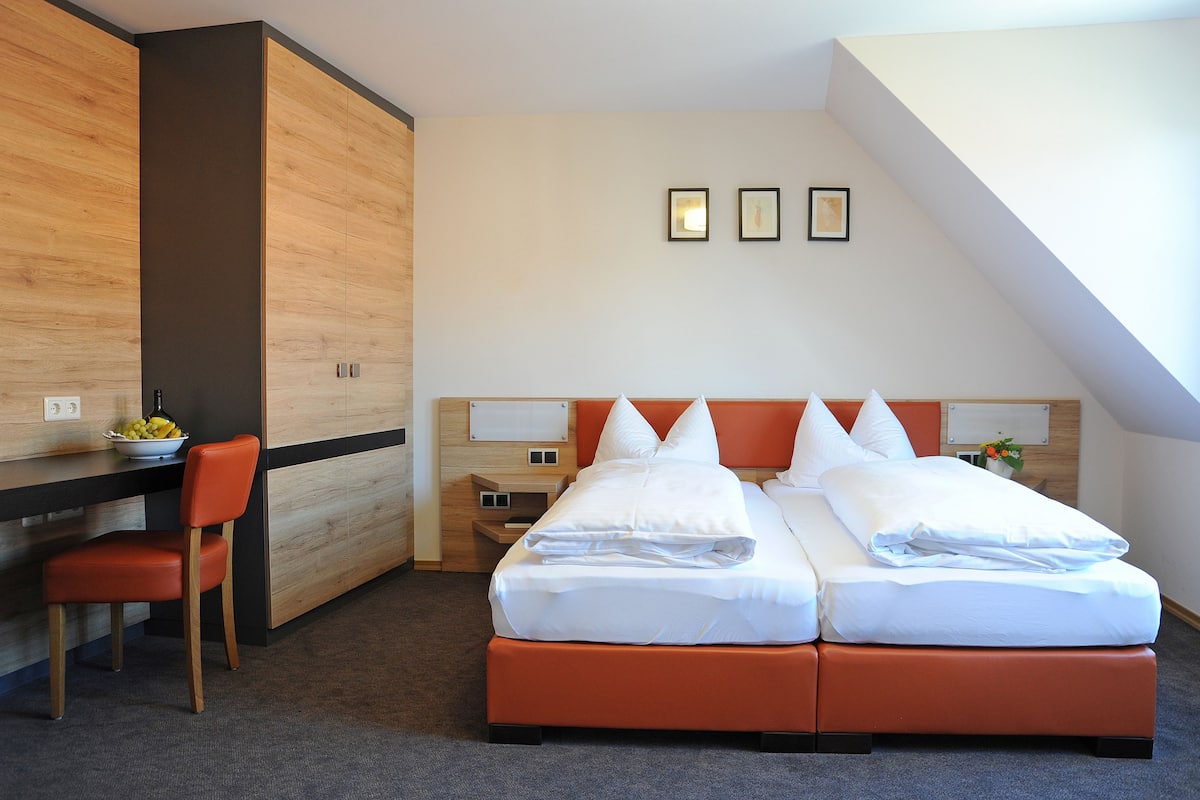 A hotel room with a bed, a desk, and a chair. There are three framed pictures on the wall.