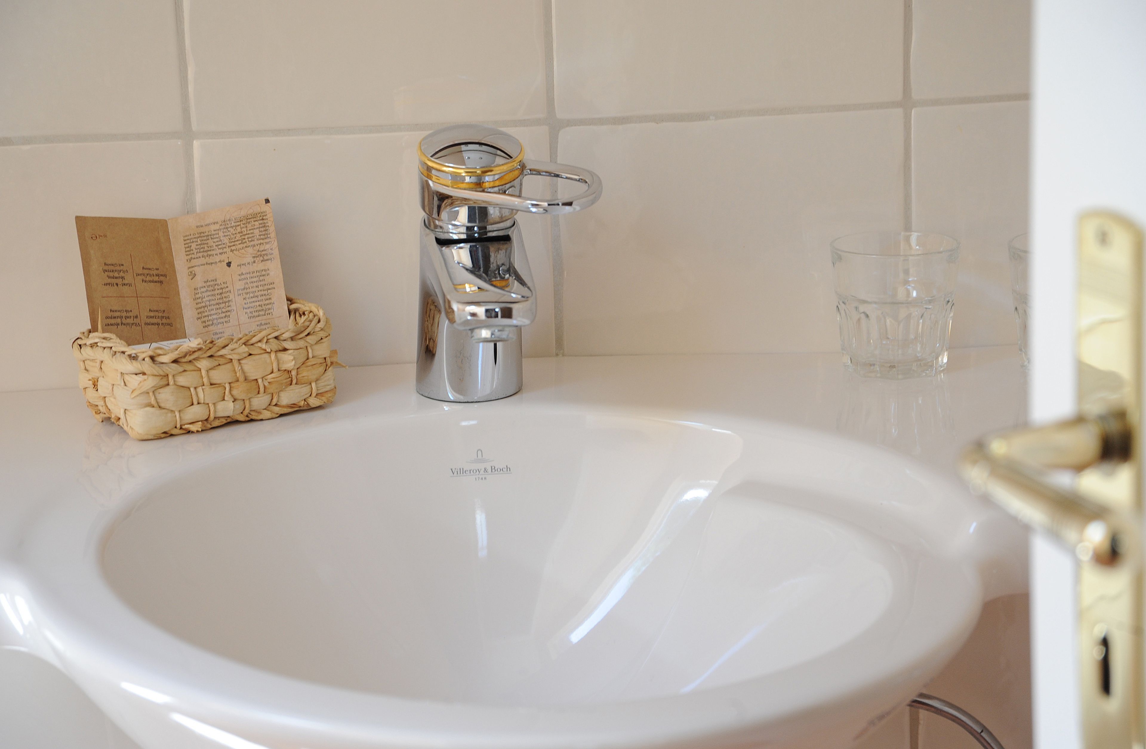 A bathroom sink with a chrome faucet, a clear glass, and a woven basket with a book.