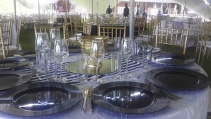 A banquet hall with round tables set for a formal event, featuring gold chairs and black table settings.