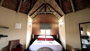 A room with a high ceiling, a bed with red pillows, a chair, a nightstand, and a mirror.
