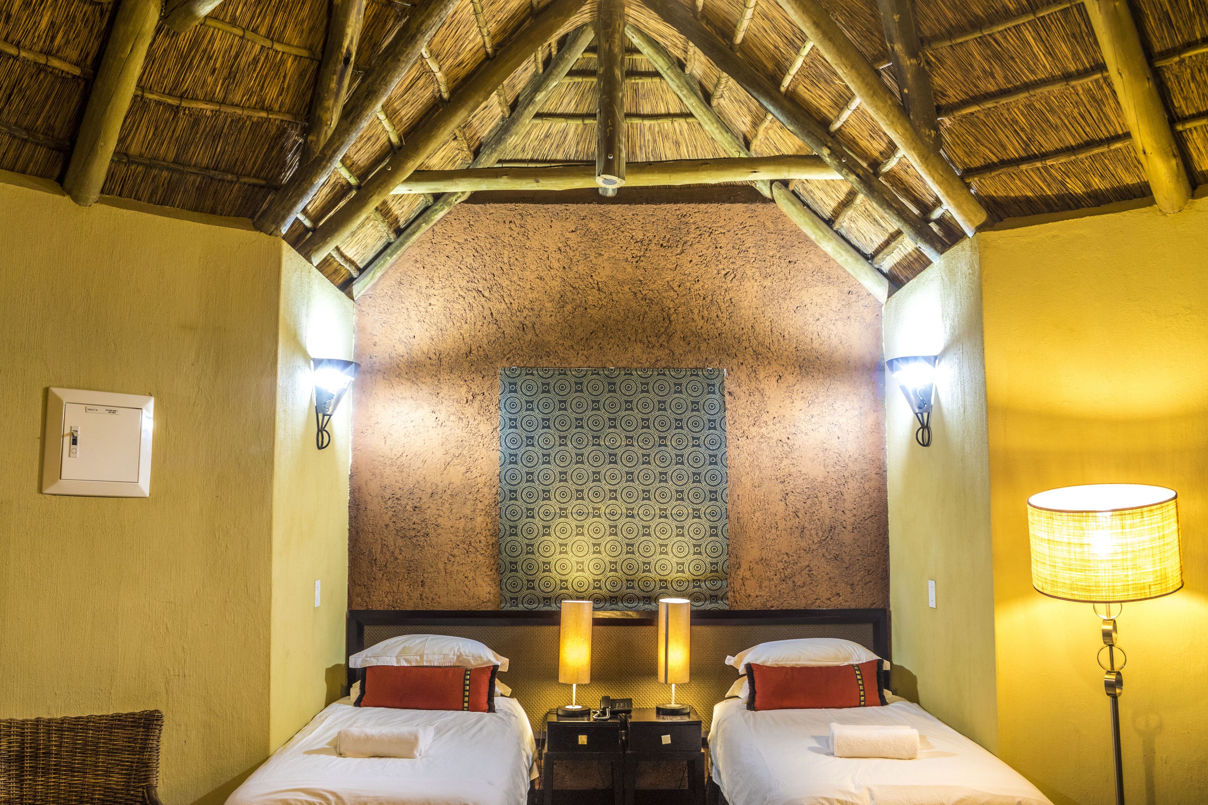 A room with two beds, a patterned tapestry, a lamp, and a wooden ceiling.