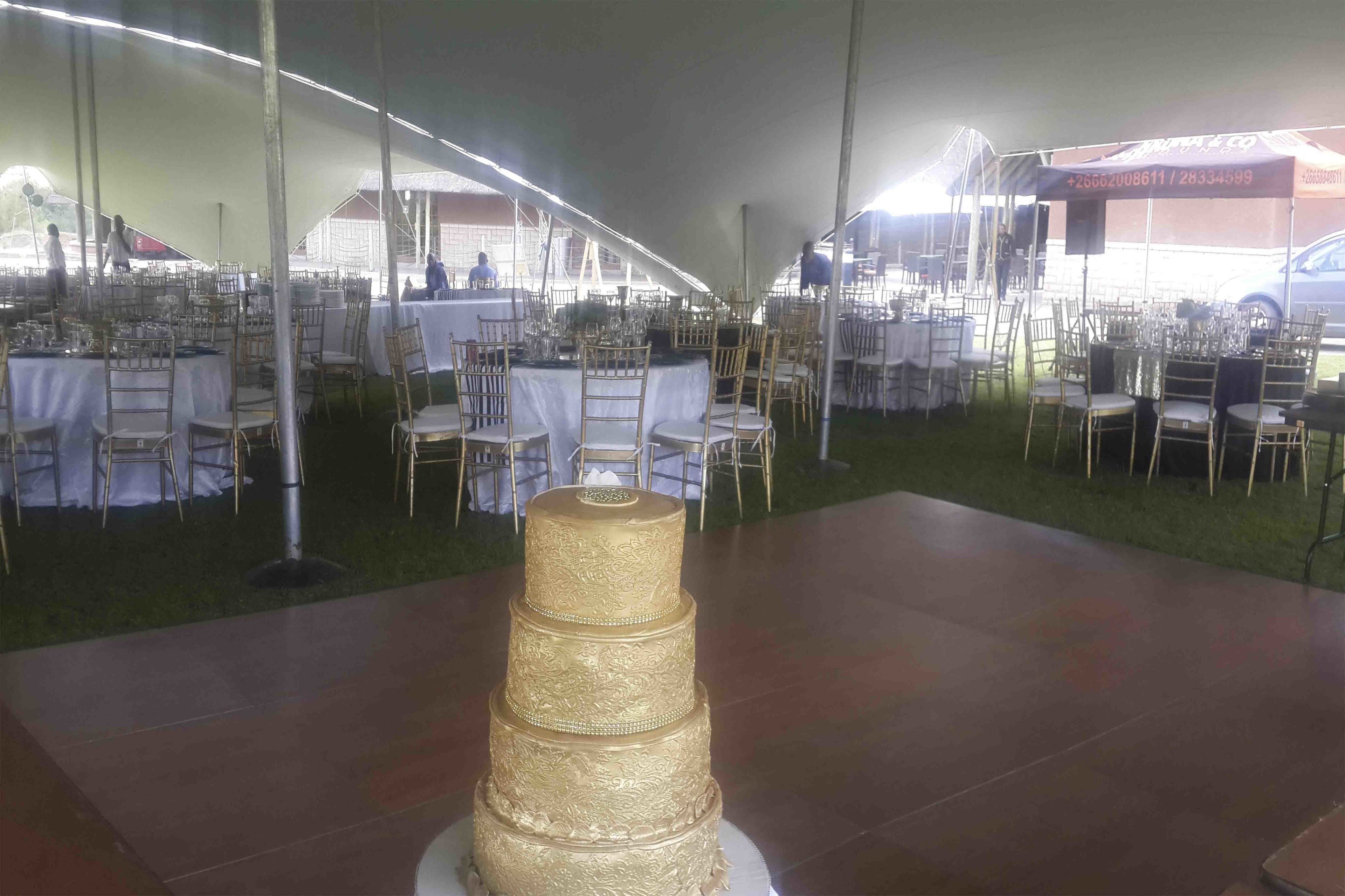 A tented event space with tables set for a formal gathering, featuring a central decorative cake.