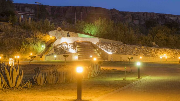 A well-lit outdoor area with a staircase leading to a building, surrounded by rocks and vegetation.