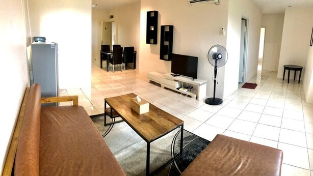 A modern living room with a sofa, coffee table, TV, and a dining area in the background.