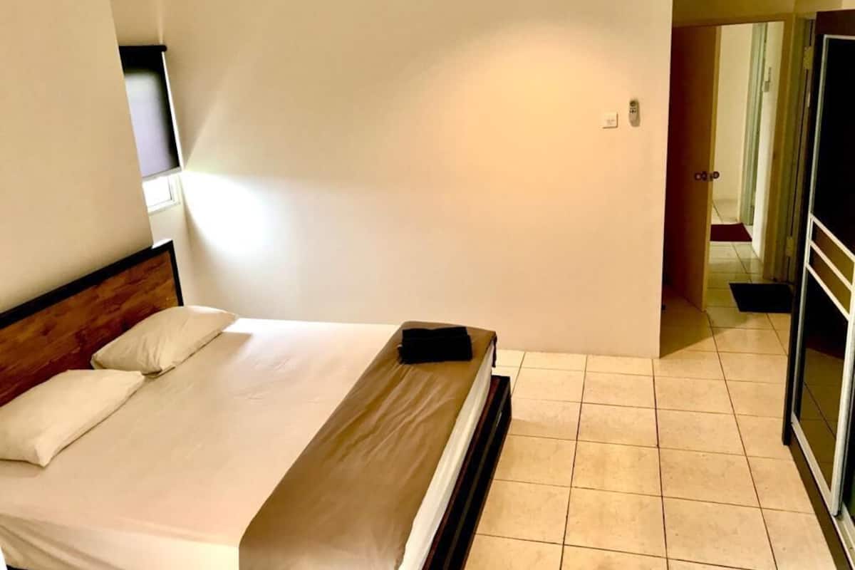 A hotel room with a bed, a small window, a door, and a tiled floor.