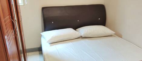 A hotel room with a bed, a wooden wardrobe, and an air conditioning unit on the wall.