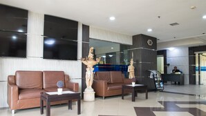 A lobby with two brown leather sofas, a coffee table, a decorative urn, and a reception desk with a receptionist.