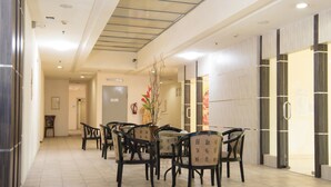 A hotel lobby with a long corridor, a reception desk, and several chairs arranged in a row.