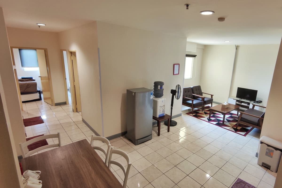 A hotel room with a dining area, a water dispenser, a fan, a TV, and a bed in the background.