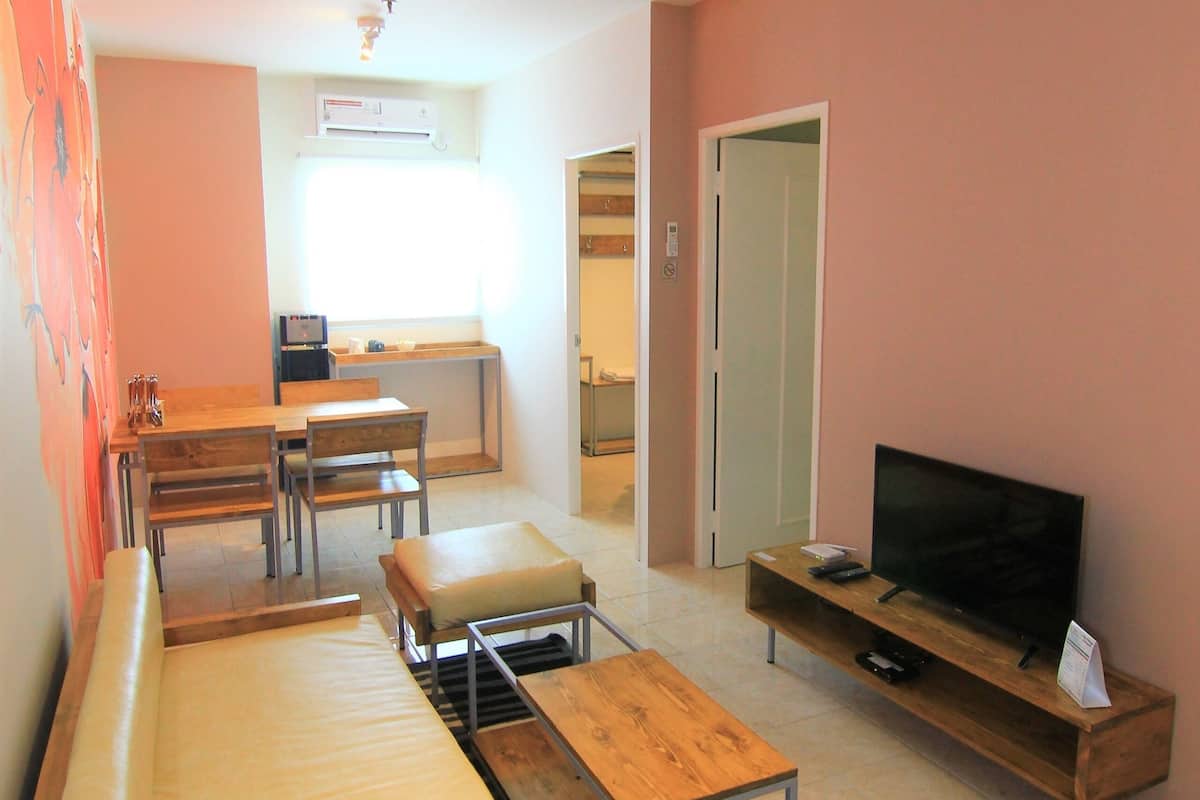 A compact living space with a sofa, a TV, a dining table, and a kitchen area.