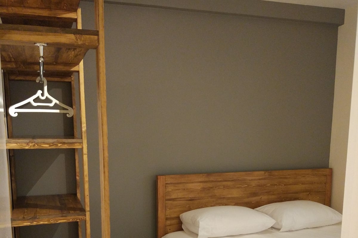 A bedroom with a wooden headboard, a bed with white linens, and a wooden wardrobe with a hanging rack.