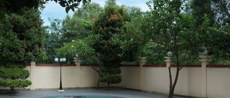 A swimming pool with a curved design, surrounded by a tiled patio and a low wall.