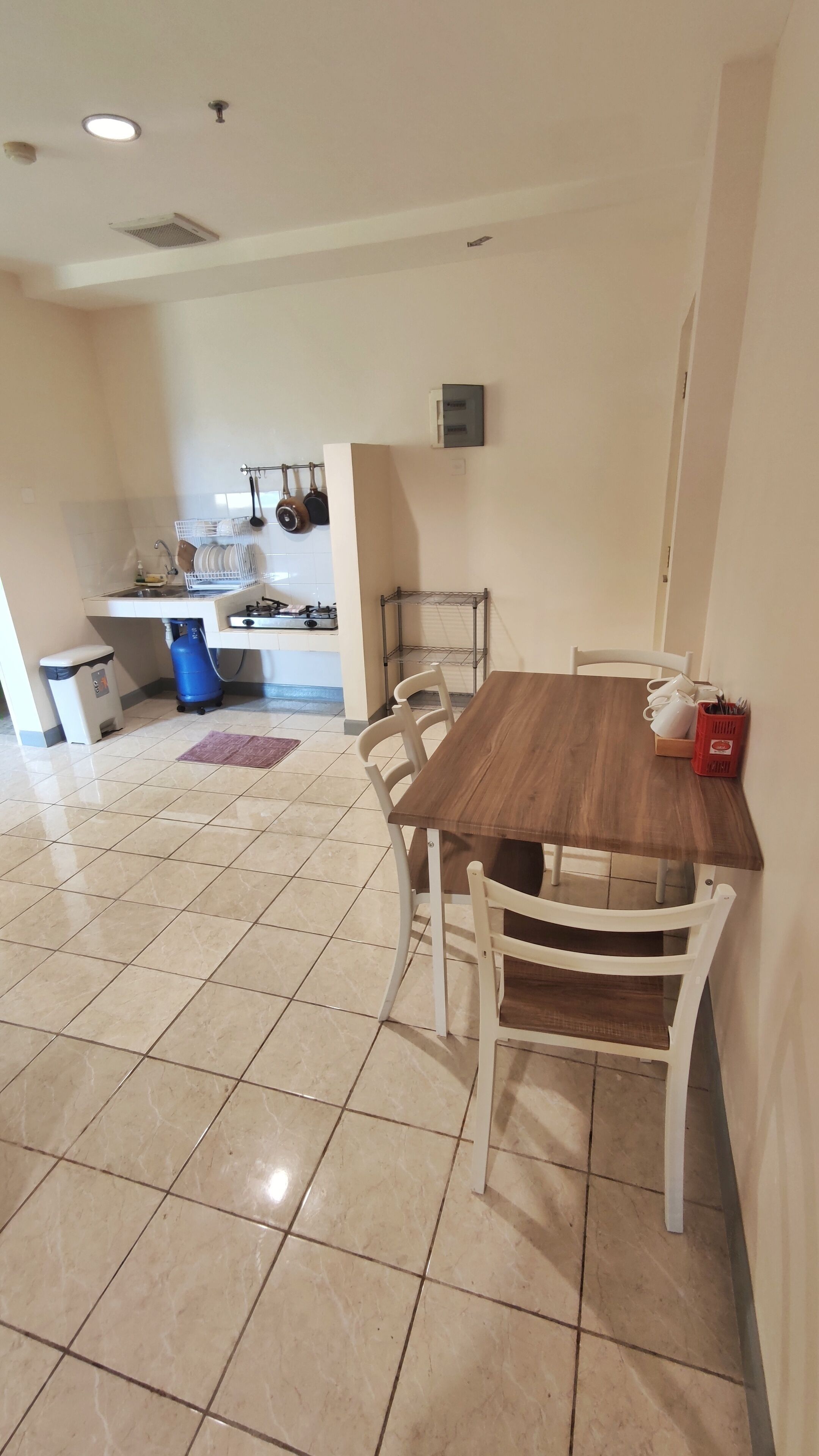Un comedor con mesa de madera y sillas blancas, una cocina al fondo y piso de baldosas.