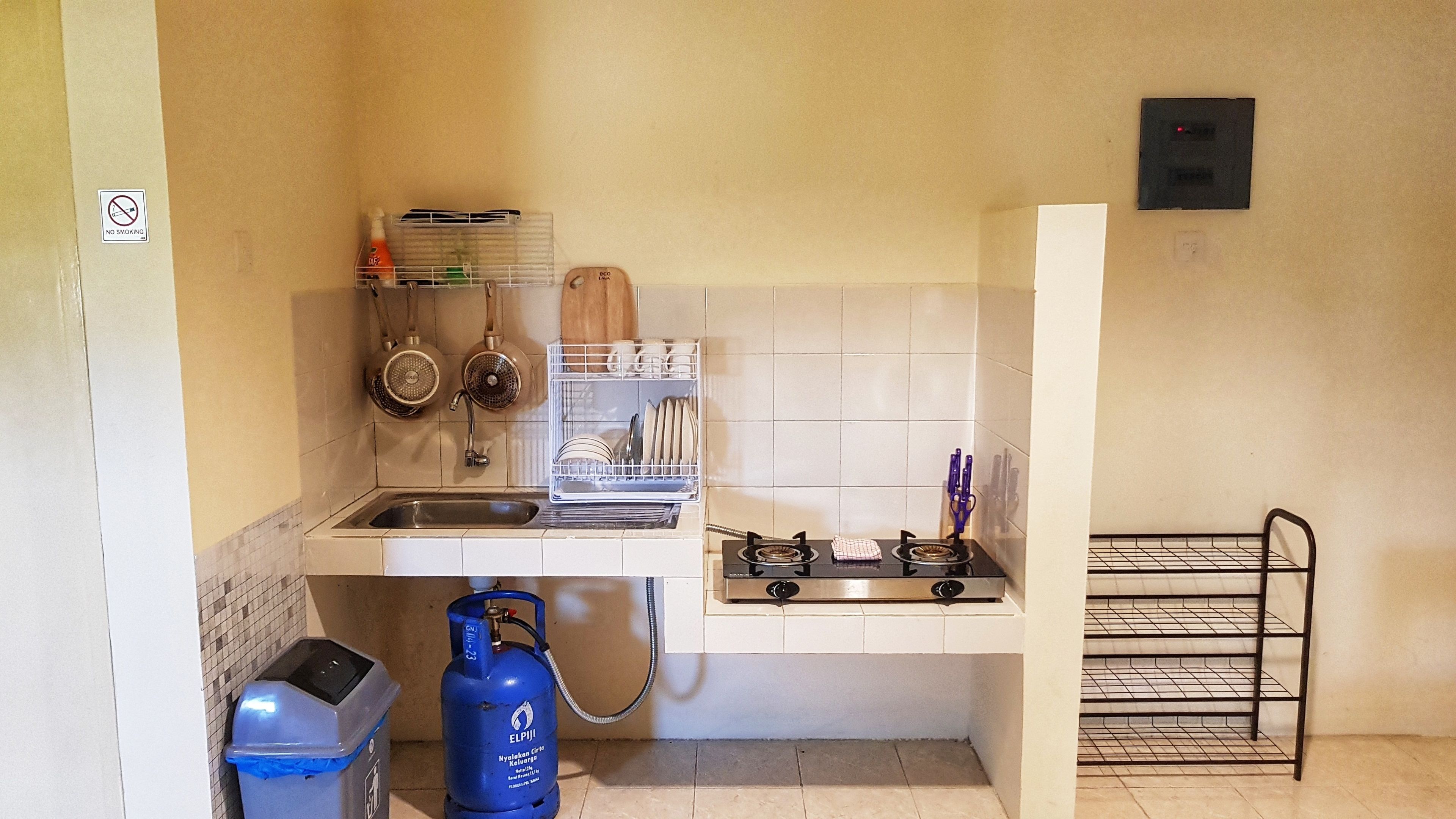 Cozinha compacta com pia, fogão e escorredor de louça. Há um botijão de gás e uma lixeira.